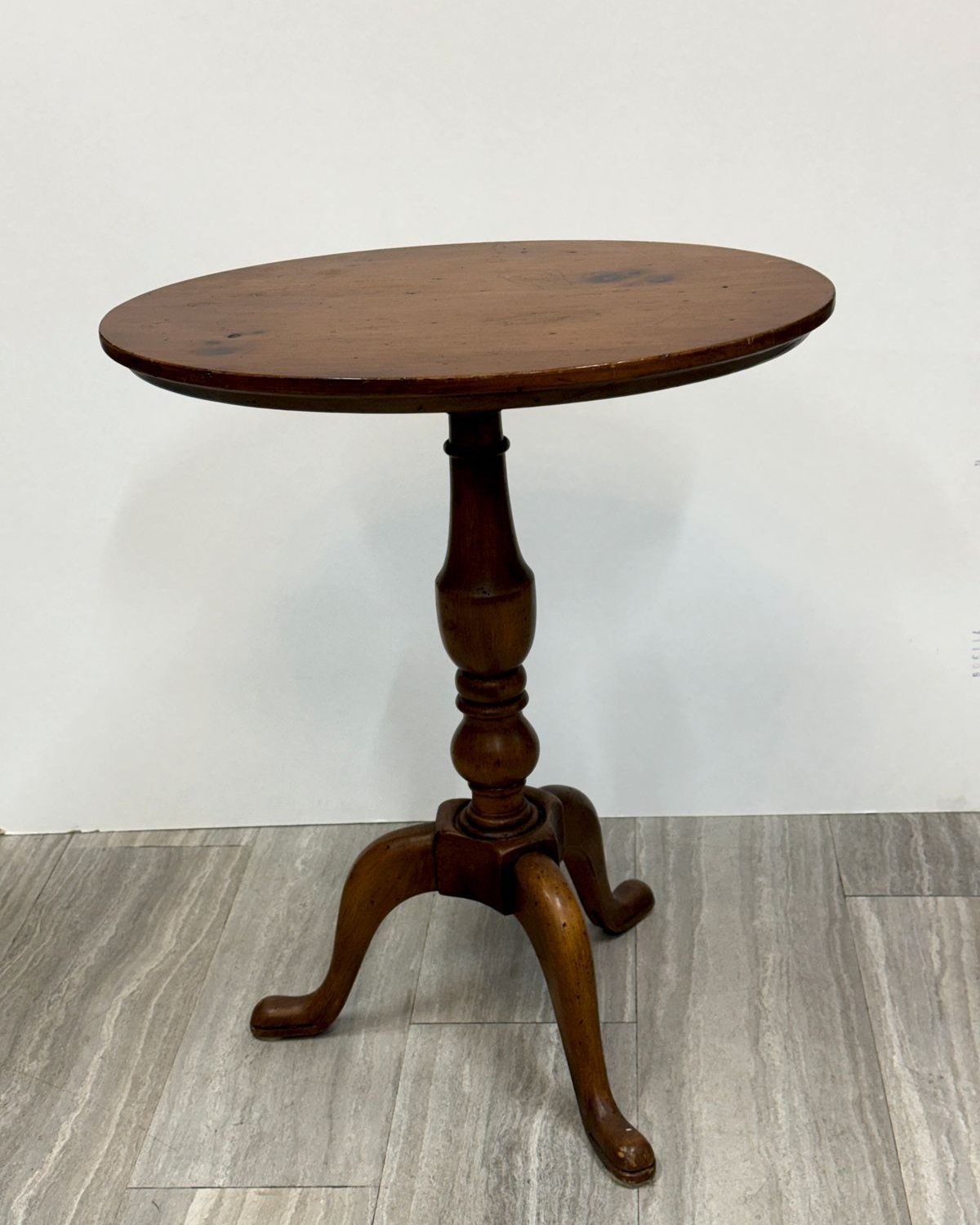 Small oval-top antique wood tilt-top table with turned pedestal and three cabriole legs ending in pad feet, warm brown patina