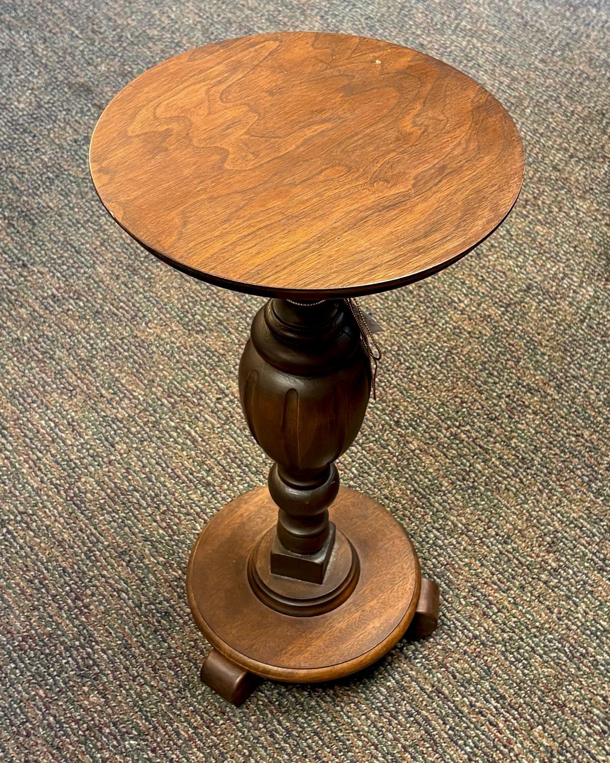 A small vintage 1970s turned-wood pedestal stand with a 13-inch round top and ornately carved baluster column rising about 24 inches tall, finished in a warm medium-brown stain.