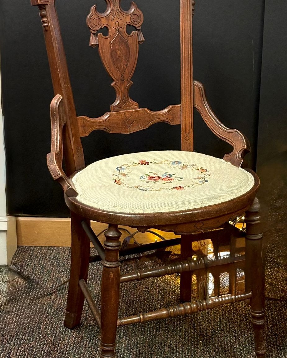 Antique Victorian carved wooden side chair with incised crest rail, urn-shaped center splat, turned spindle legs, and an oval floral needlepoint seat.