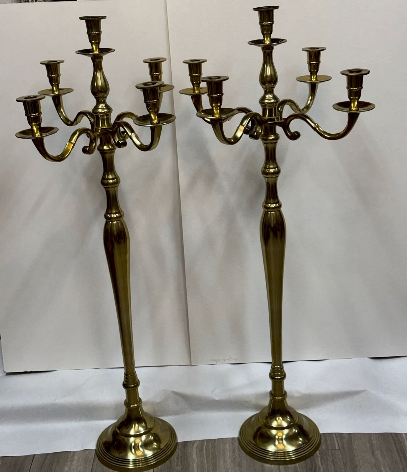 A matched pair of tall polished brass five-light candelabras, each about 42 inches high, with turned baluster stems, scrolled arms holding bobeche cups around a taller central candle holder, and weighted stepped round bases.